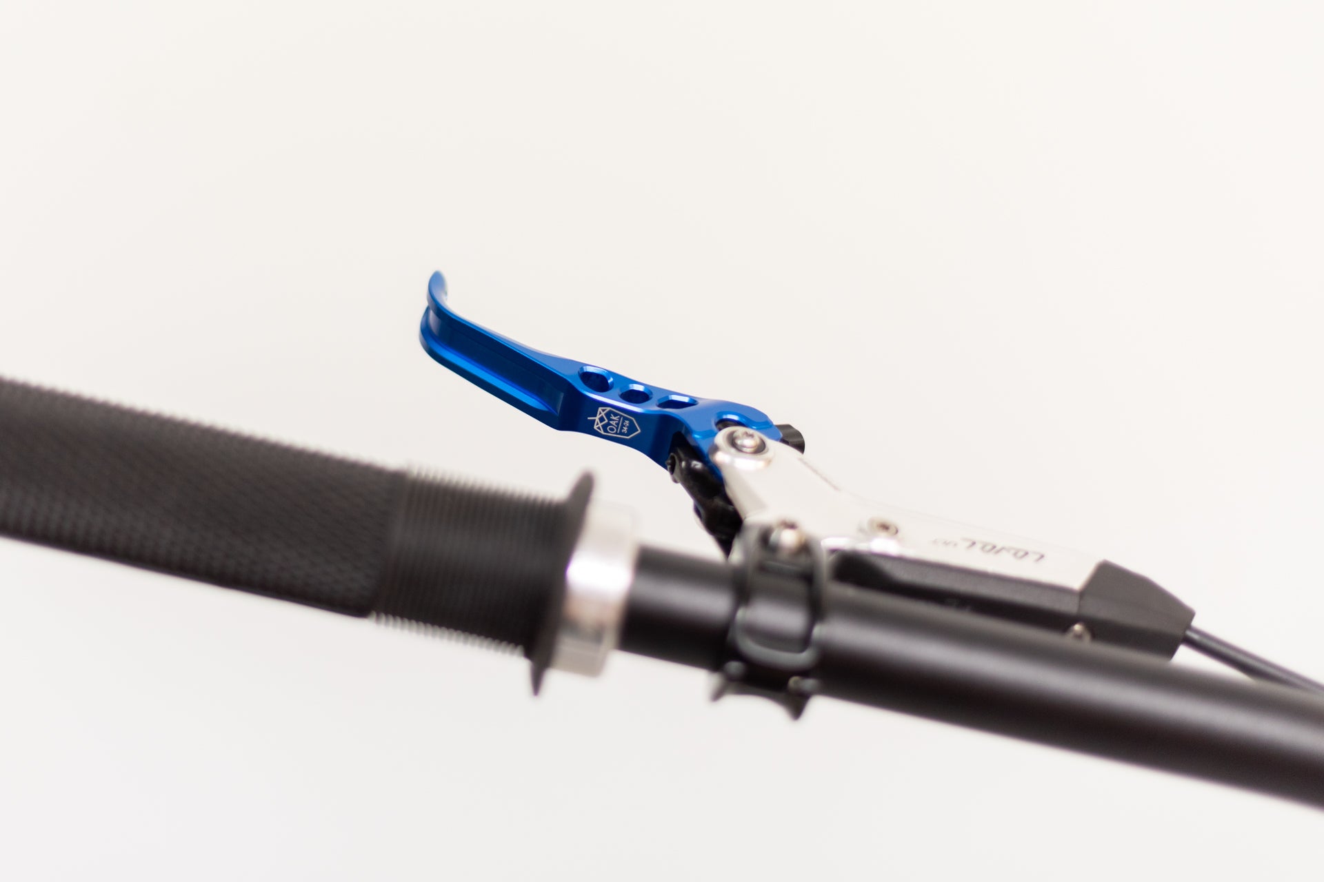 Close-up of a blue metallic OAK MAX brake lever and silver LOLOU brake housing on a black textured bicycle handlebar grip.
