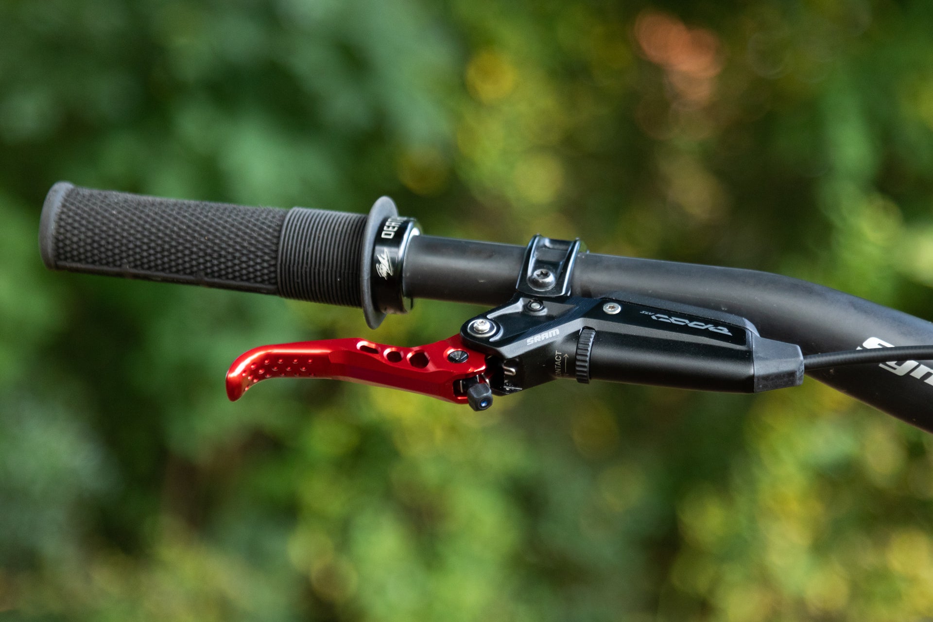 Close-up of a black mountain bike handlebar with SRAM brake lever and red anodized drilled lever.