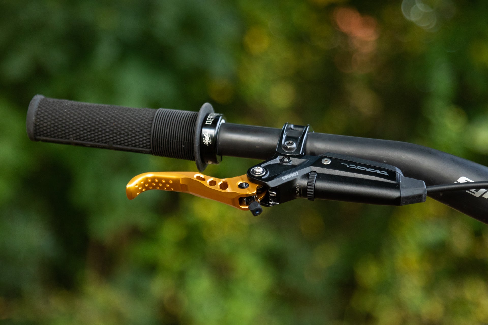 Golden perforated brake lever and black handlebar grip on a bicycle with SRAM branding against green foliage
