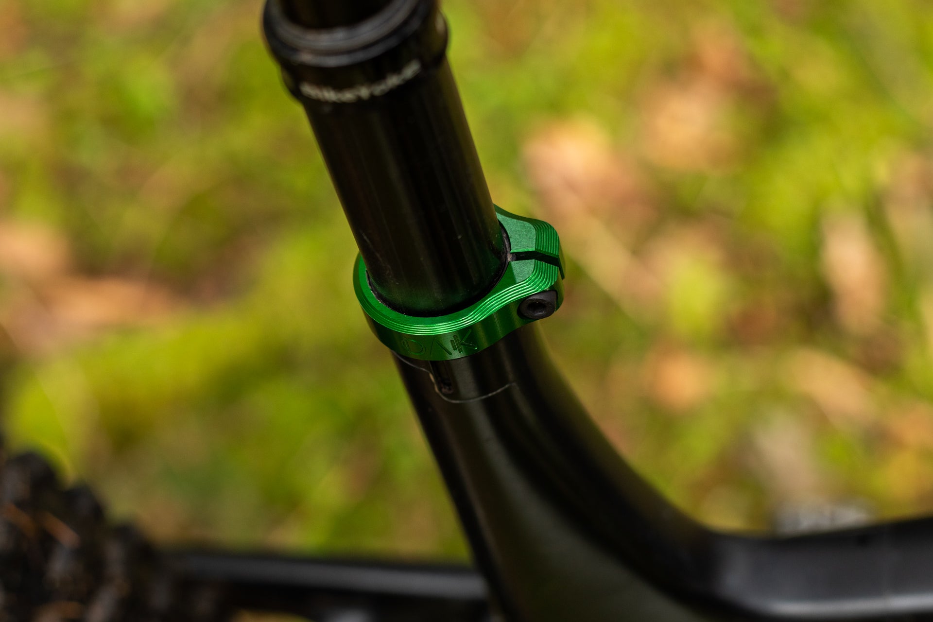 Green metallic bicycle seatpost clamp on black seatpost and frame with blurred background.