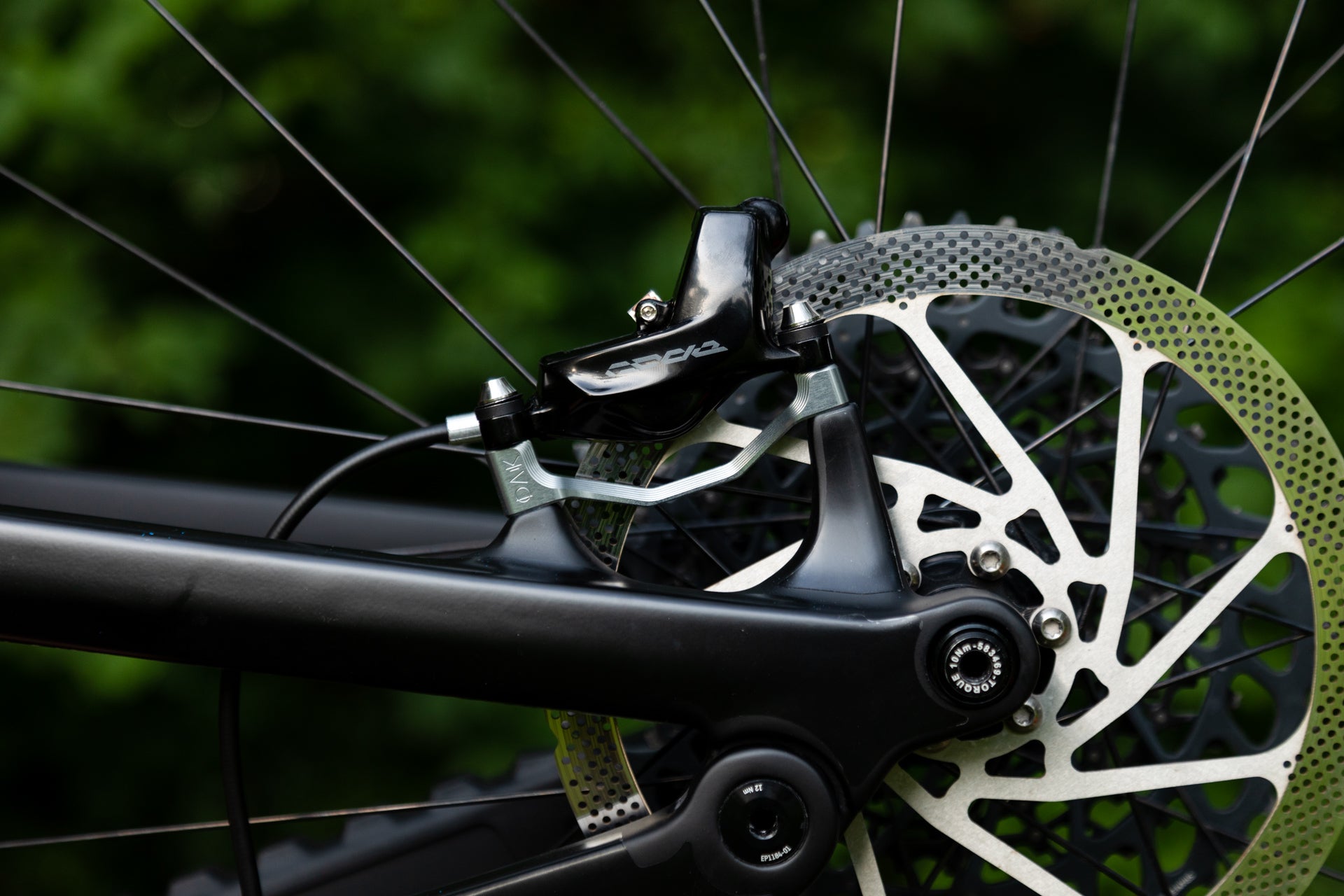 Close-up of a rear bicycle disc brake caliper EP1184-01 on a matte black frame with perforated rotor.