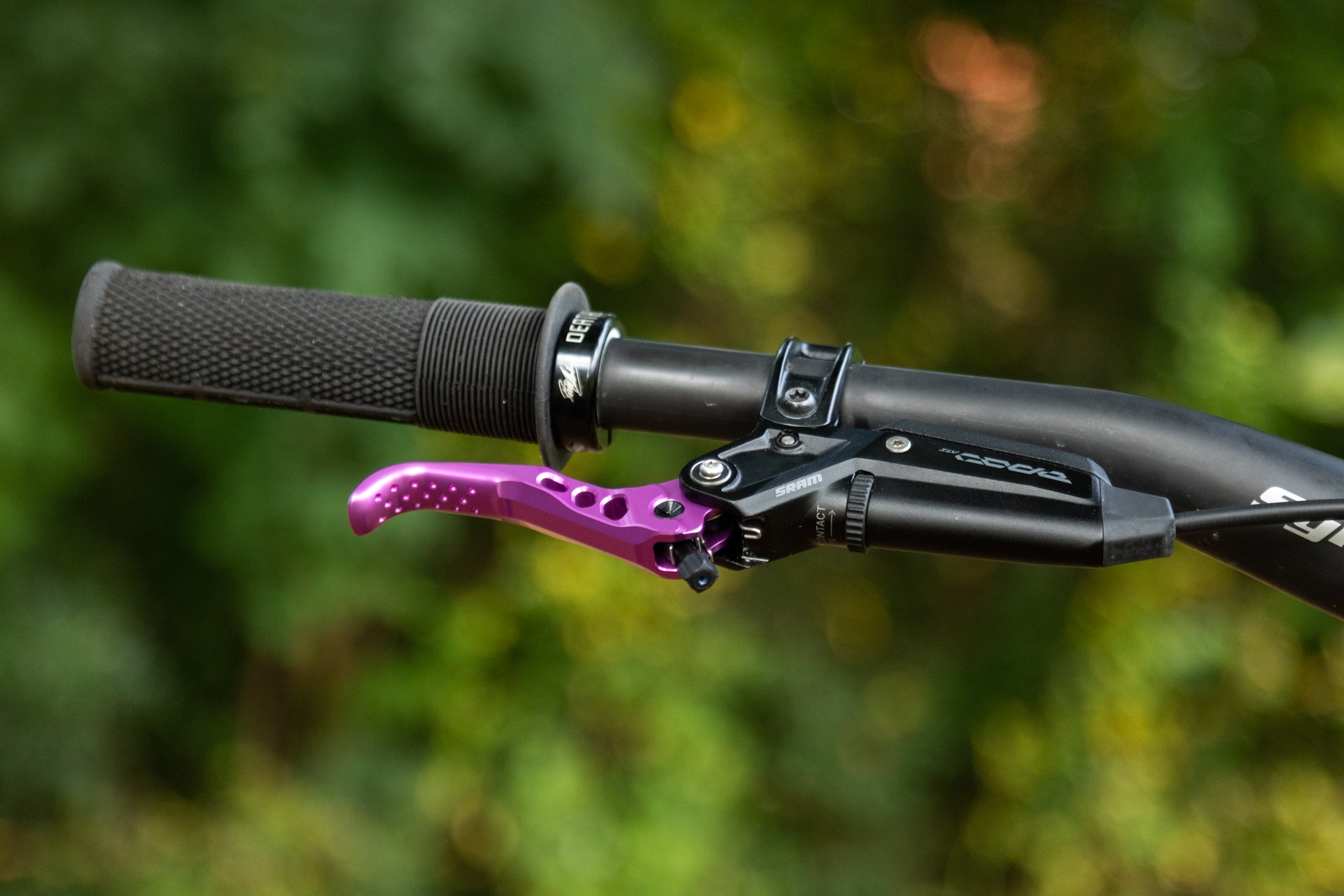 Close-up of mountain bike handlebar with black grip and purple brake lever.