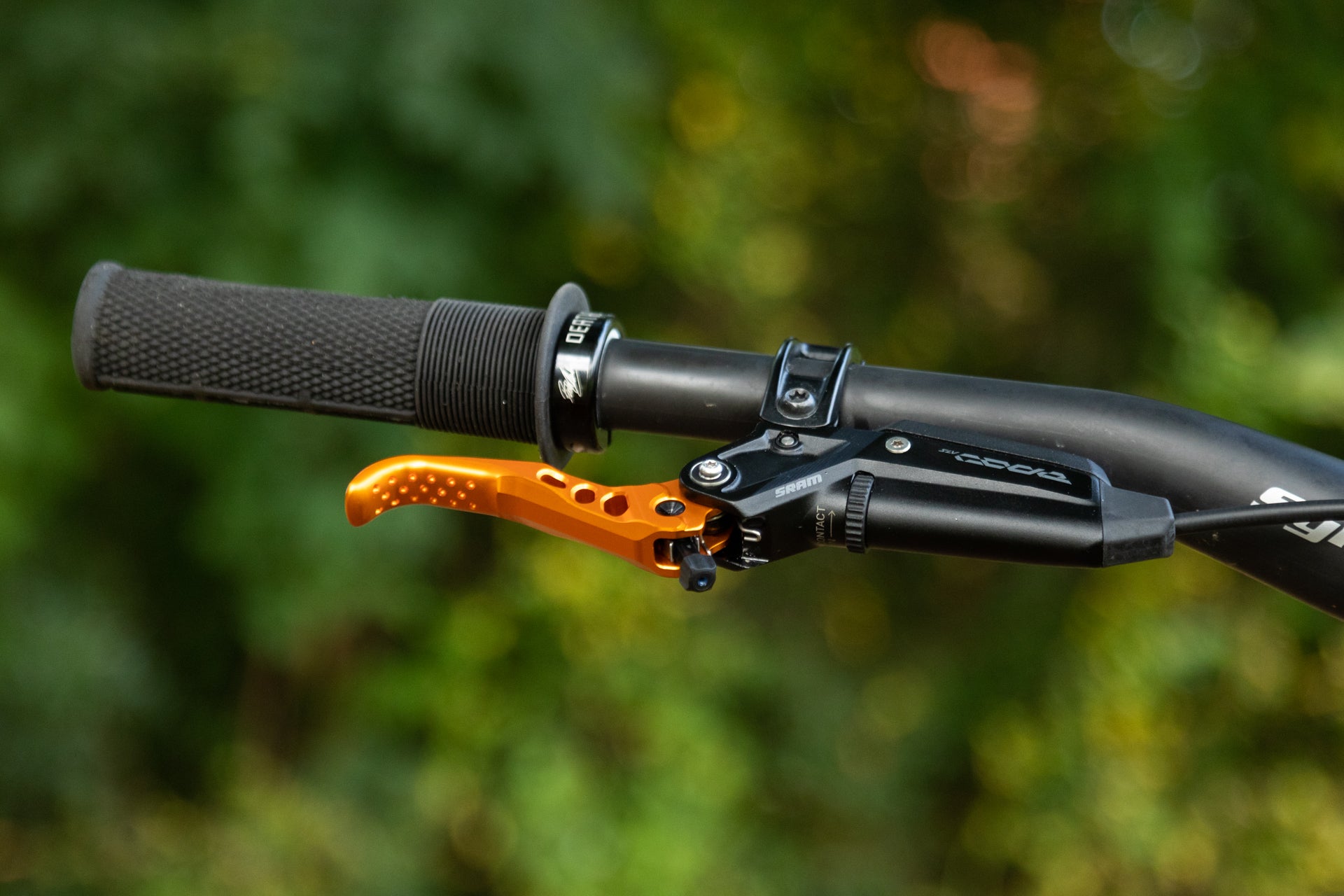 Close-up of a mountain bike handlebar with black rubber grip and orange SRAM brake lever