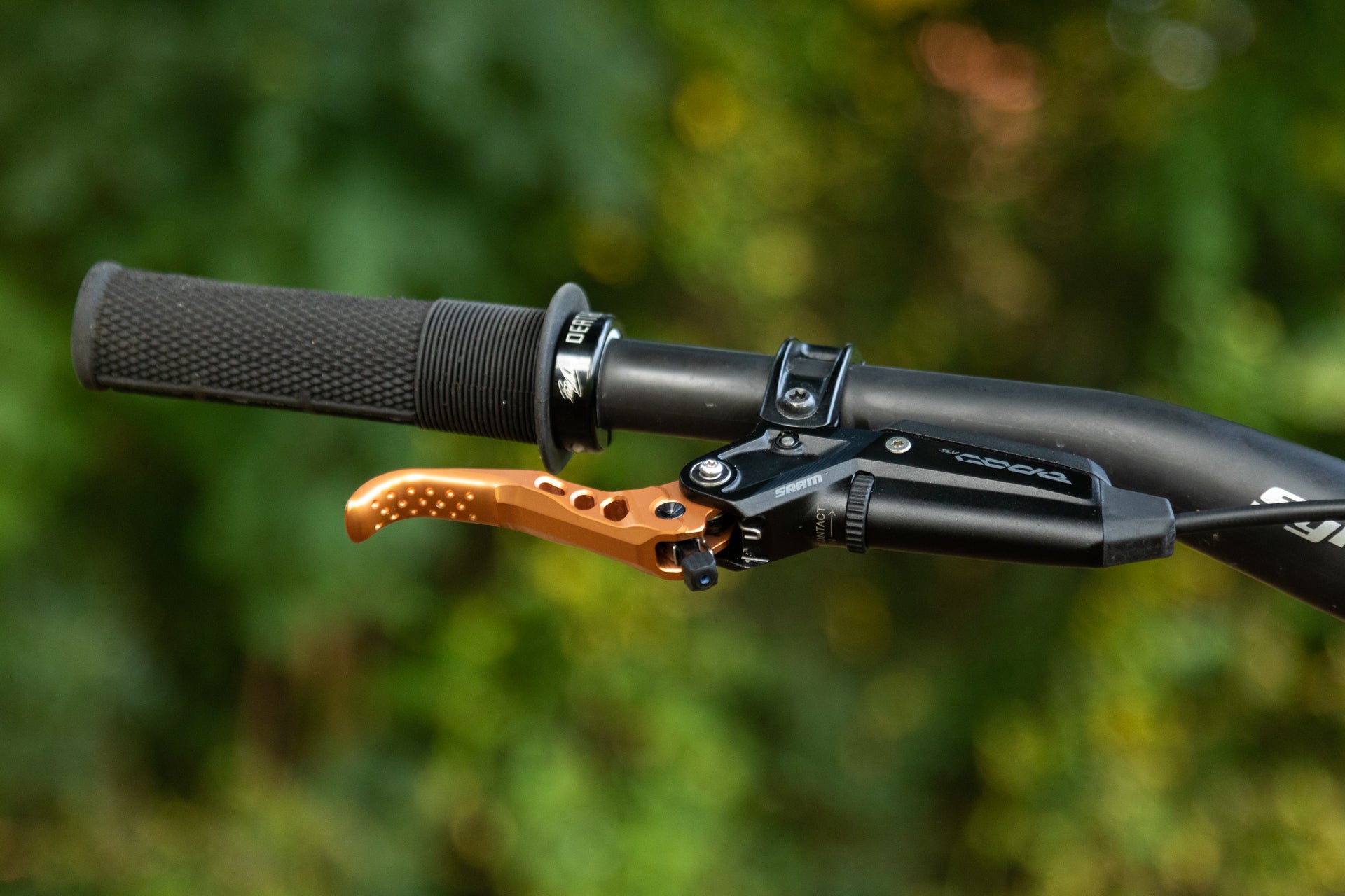 Black mountain bike handlebar with textured grip and orange SRAM brake lever for performance cycling.