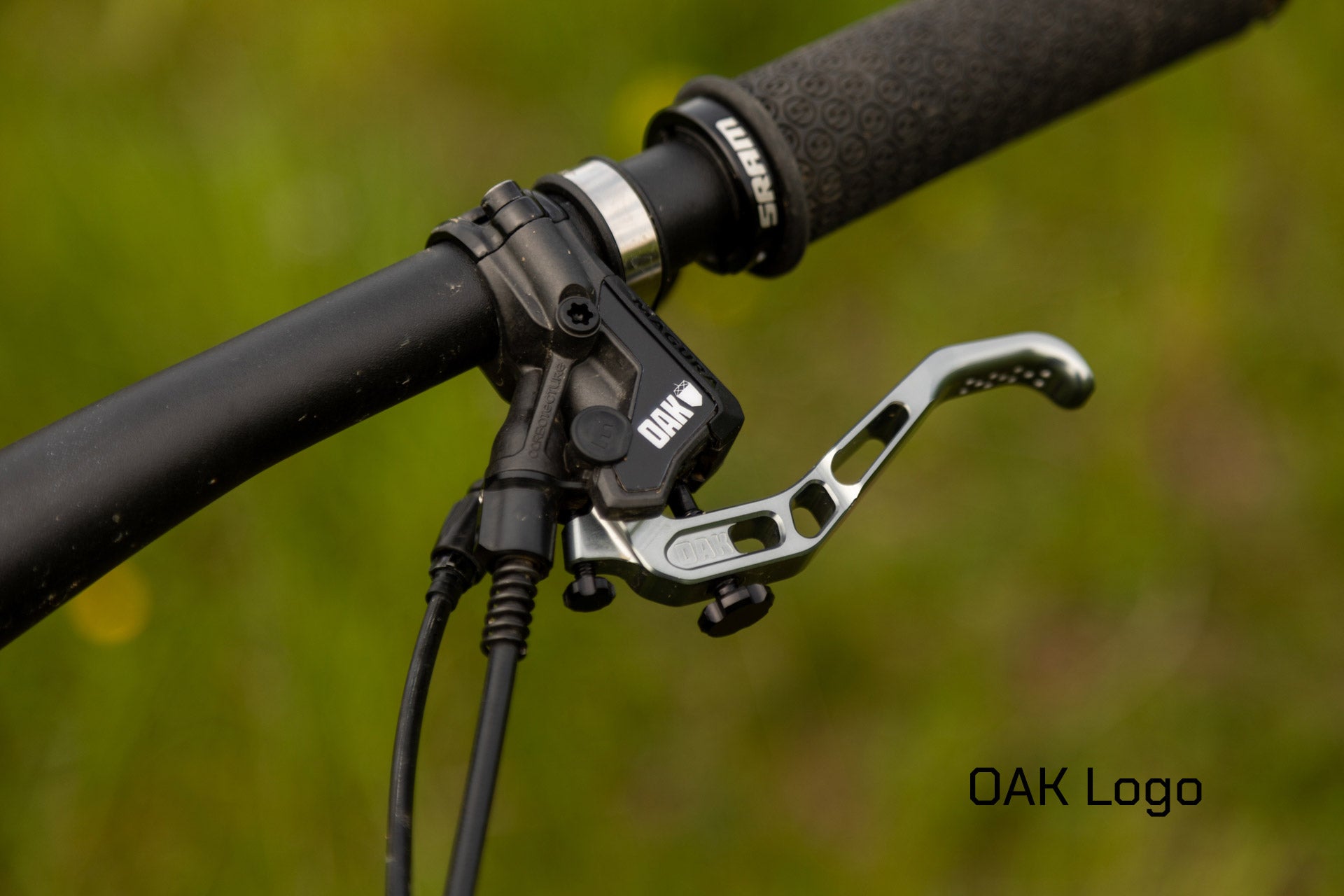 Close-up of mountain bike handlebar with black hydraulic brake lever branded OAK and textured SRAM grip.