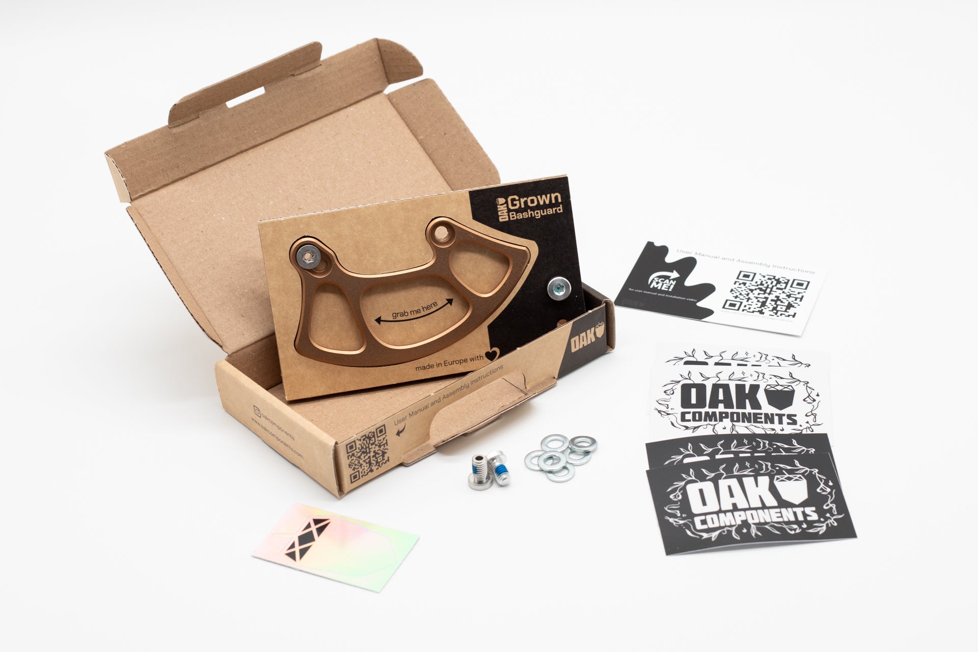 Bronze metal bashguard in an open cardboard box with OAK COMPONENTS branding, assembly instructions, and hardware.