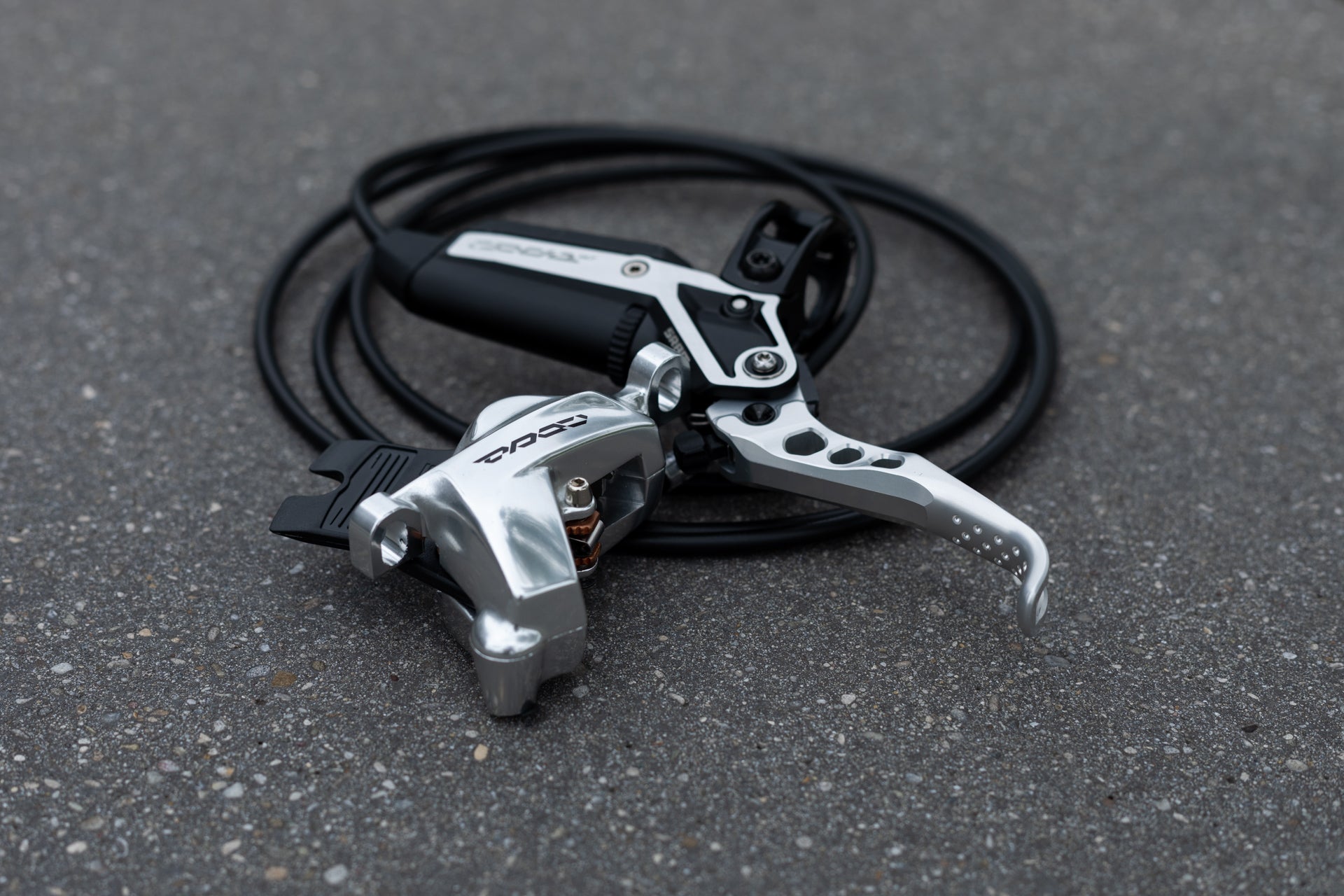 Silver and black Zoom bicycle hydraulic brake lever and caliper assembly on asphalt.