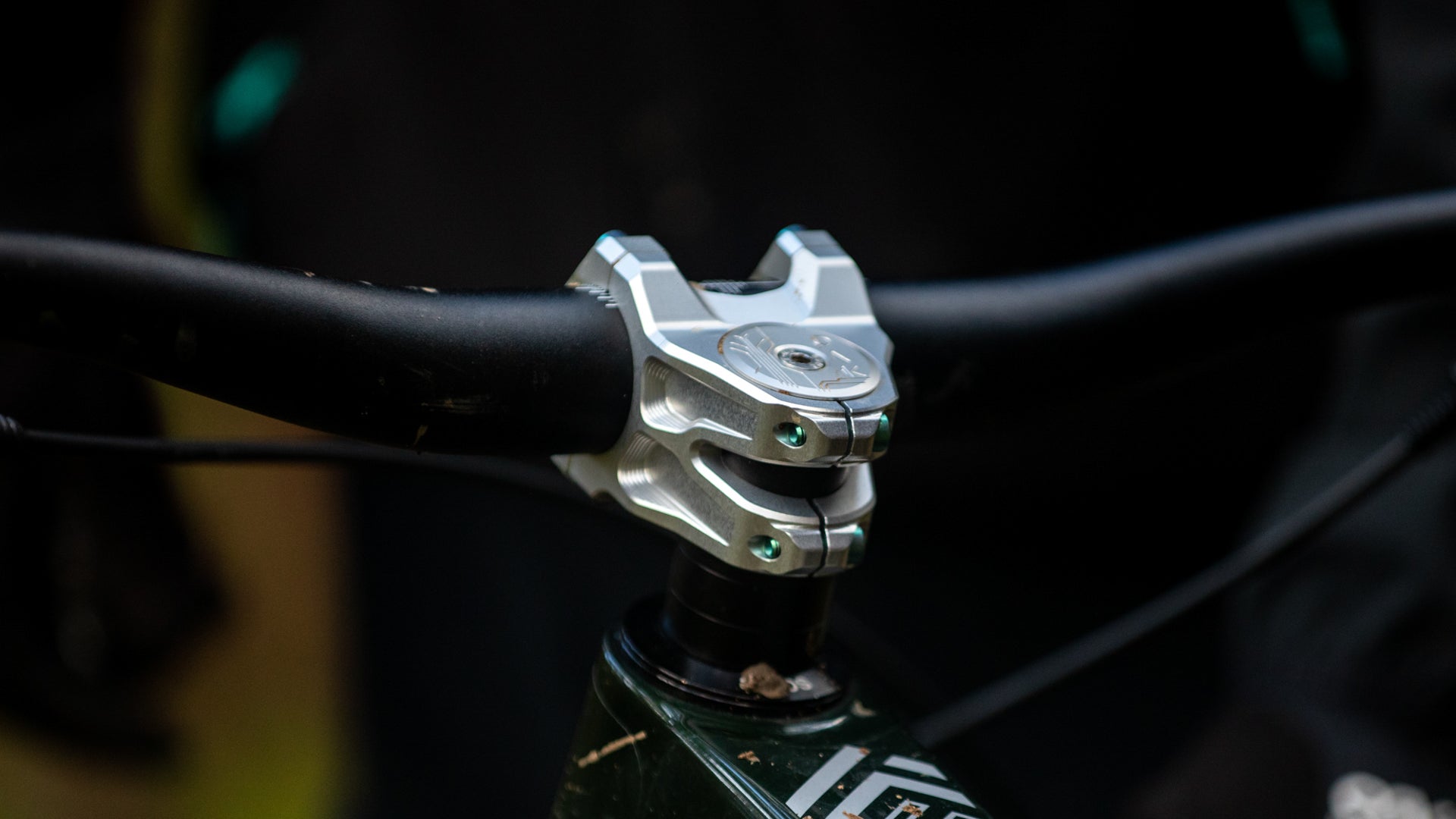 Silver stem clamp securing black handlebar on dark green mountain bike with white decal and mud splatters