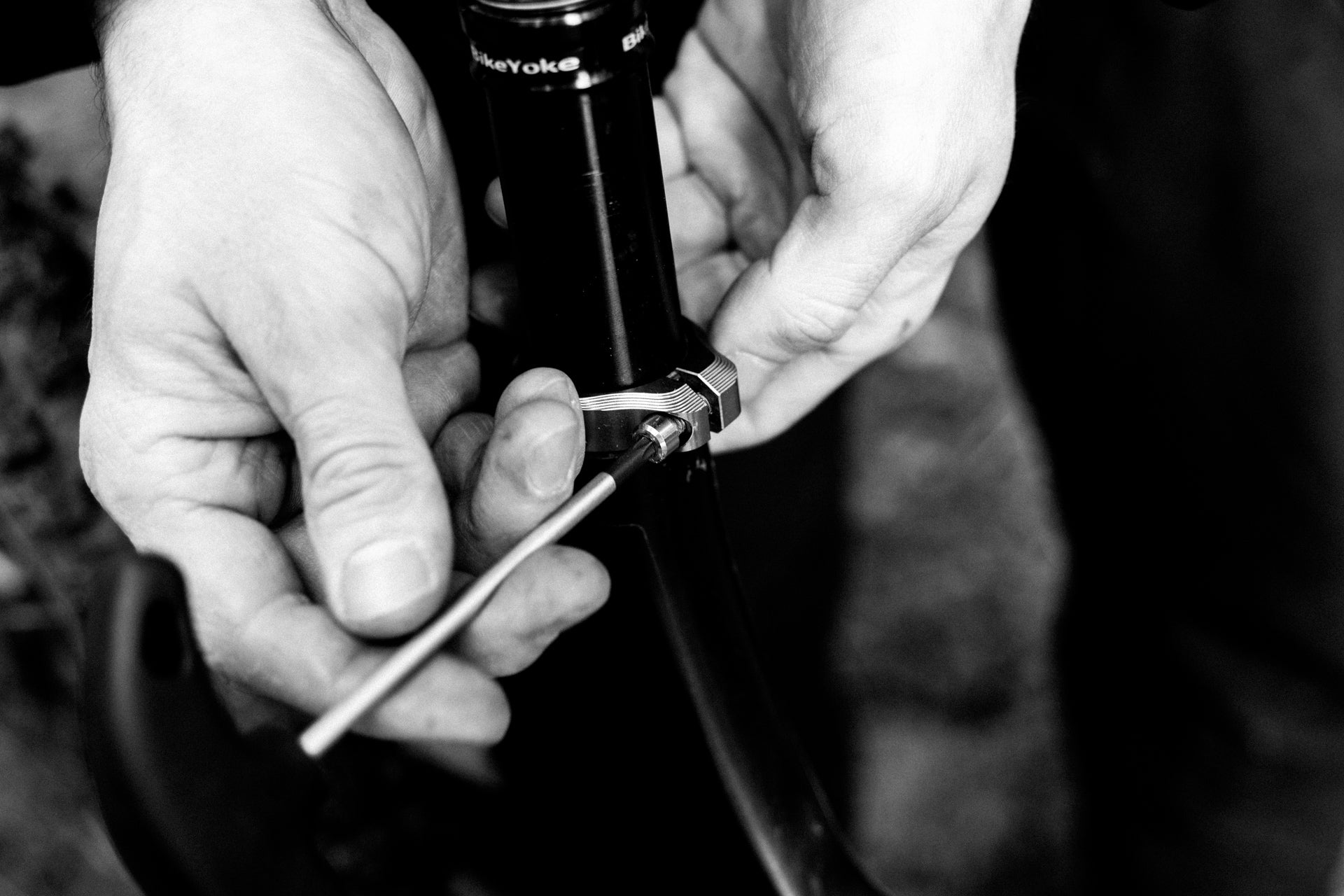 Hands tightening a bolt on a metal clamp attached to a black bicycle frame tube.