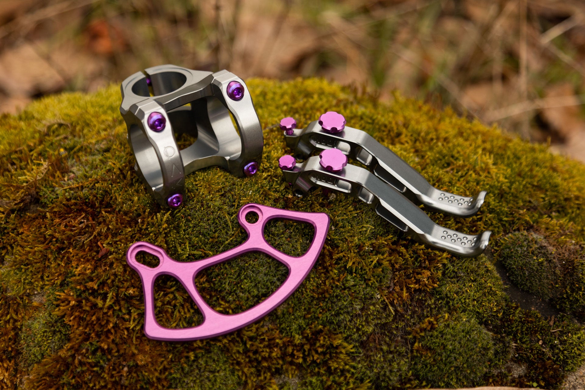 Silver bicycle stem with purple bolts, engraved 'OX' and 'AV', on moss with brake levers and purple chain guide parts.