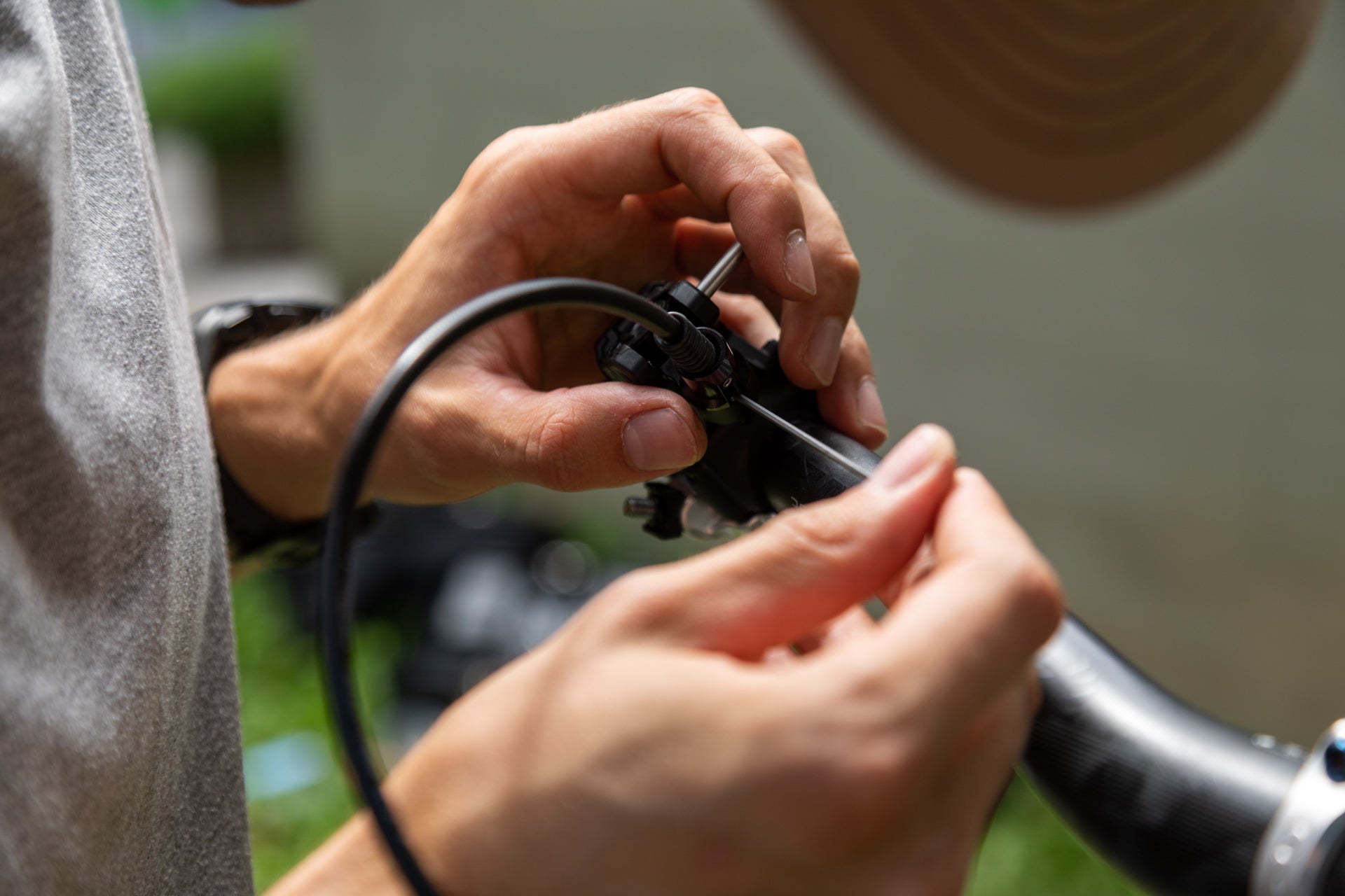 Hands adjusting a cable on a black mountain bike component, showing precision in bike maintenance