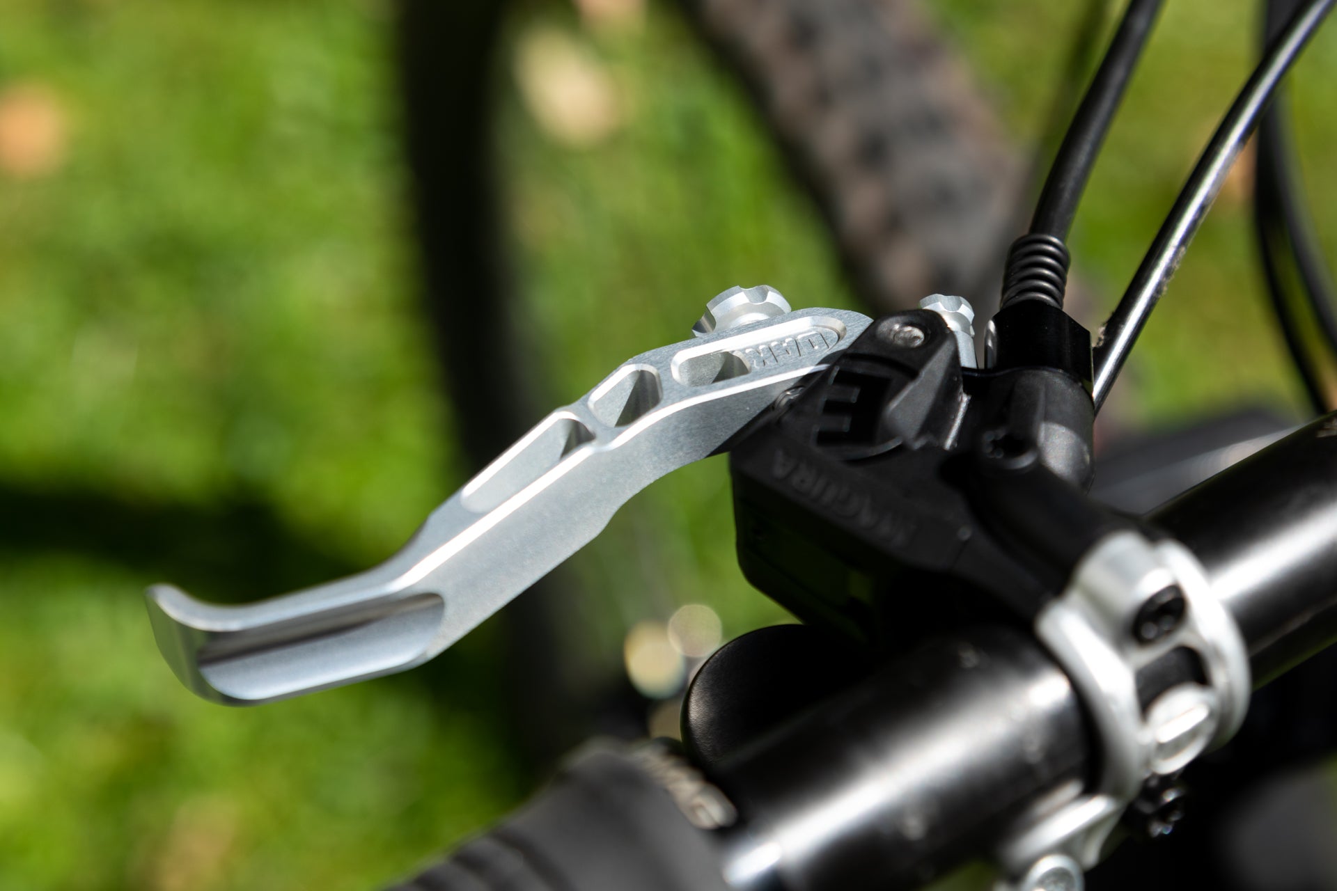 Silver MAGURA brake lever on a black bicycle handlebar with green grass in the background, highlighting its design