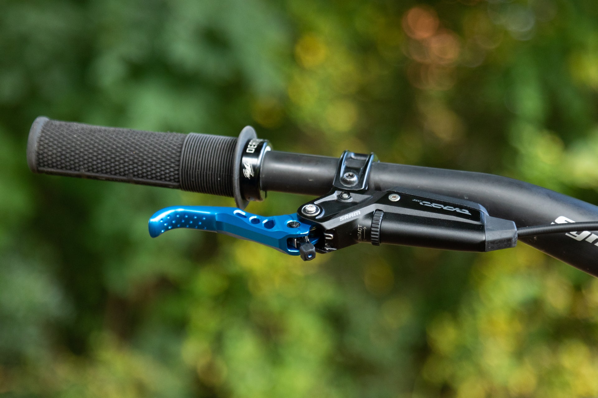 Close-up of a mountain bike handlebar with black grip and blue anodized SRAM brake lever featuring ONTACT dial