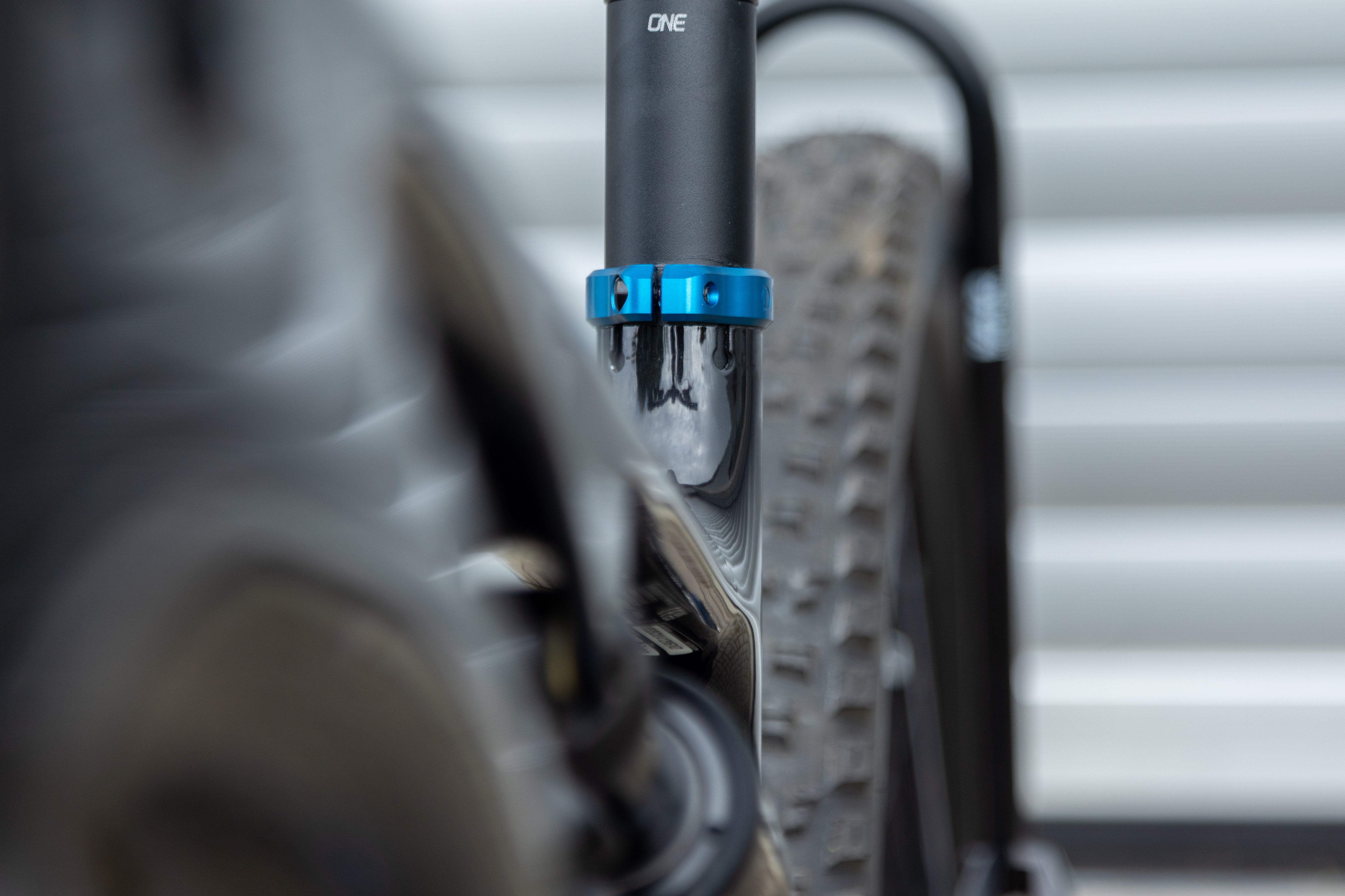 Close-up of black bicycle seat post with blue clamp labeled OAK, blurred rear tire in background.