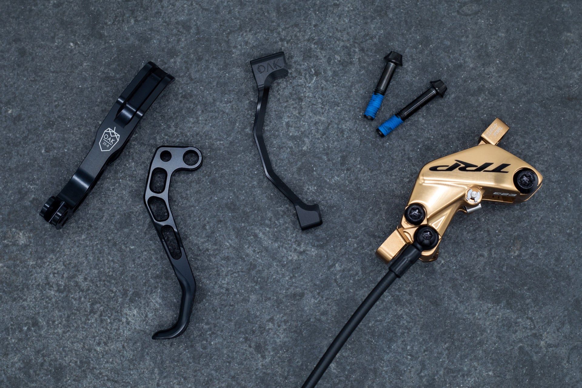 Gold TRP hydraulic bicycle brake caliper with black screws, hose, mounting levers, and bolts.