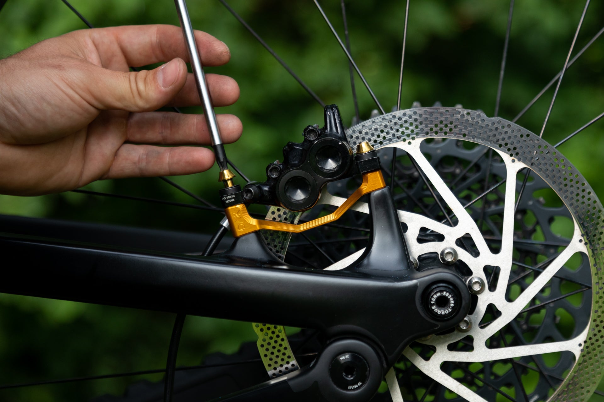 Hand adjusting gold-colored bicycle disc brake caliper on black mountain bike with silver rotor