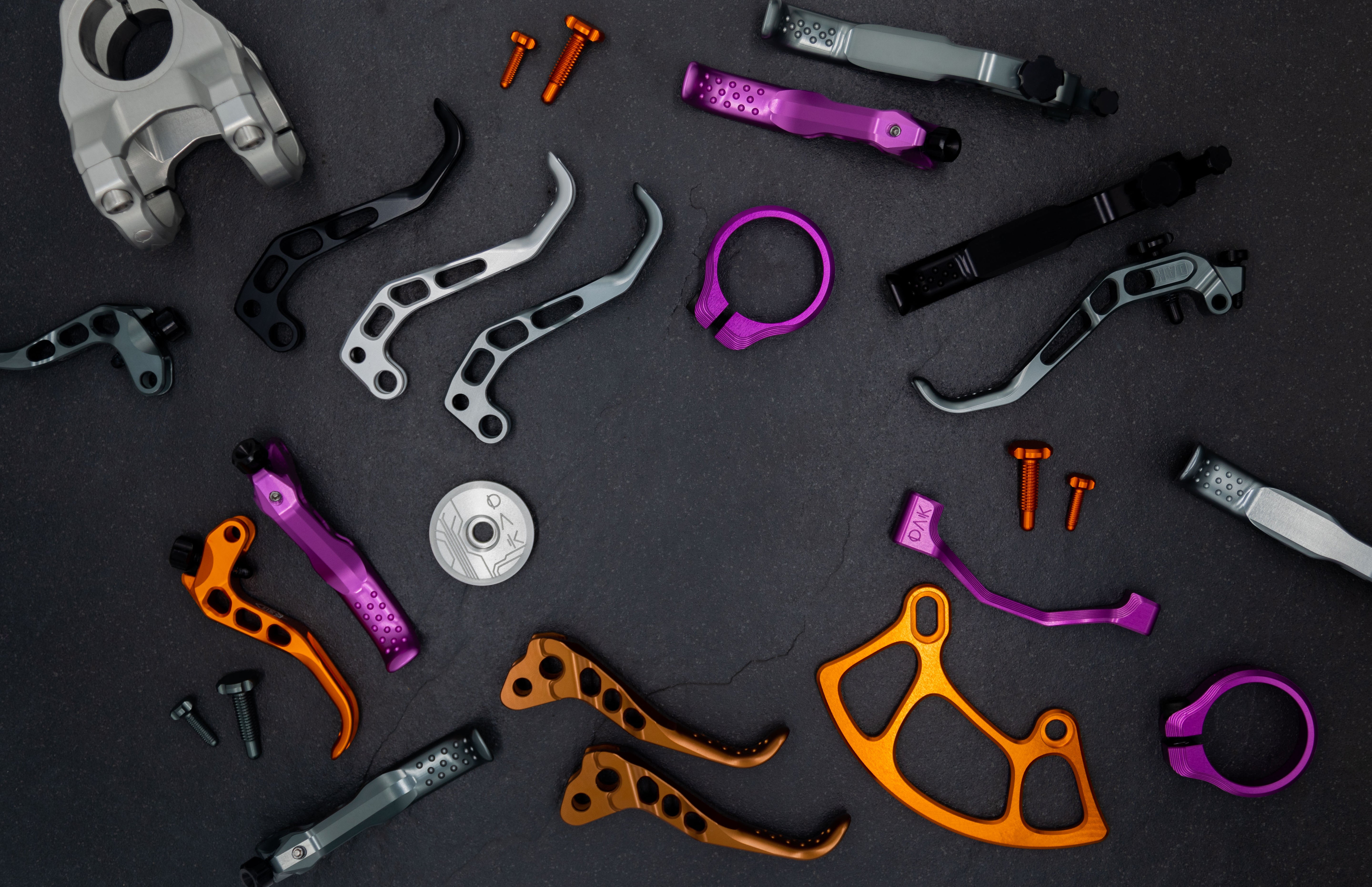 Colorful metallic mountain bike components including levers and screws on a dark surface.