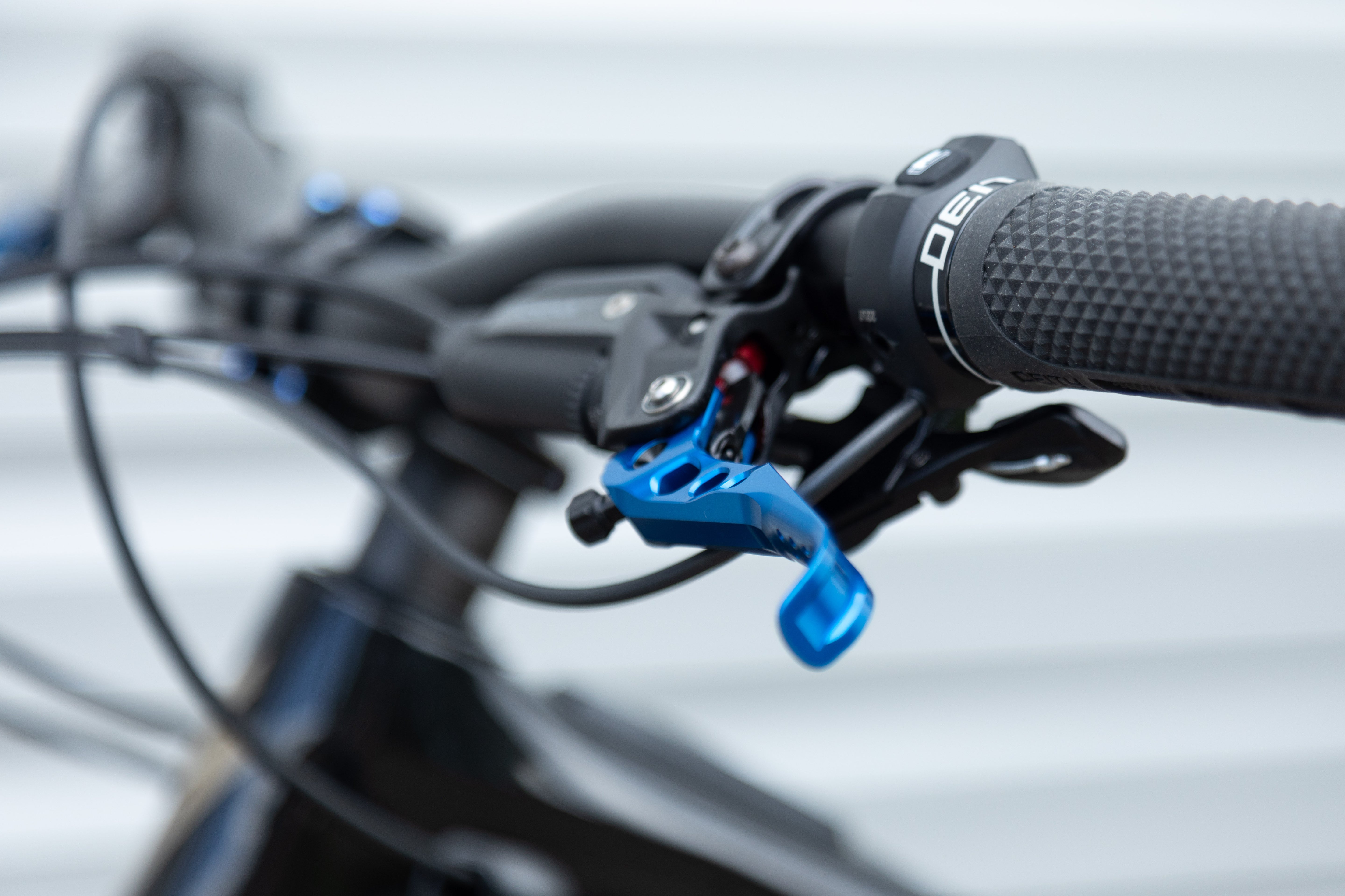 Close-up of a bicycle handlebar with textured black grip, blue metal brake lever, and OAK branding on the grip collar.