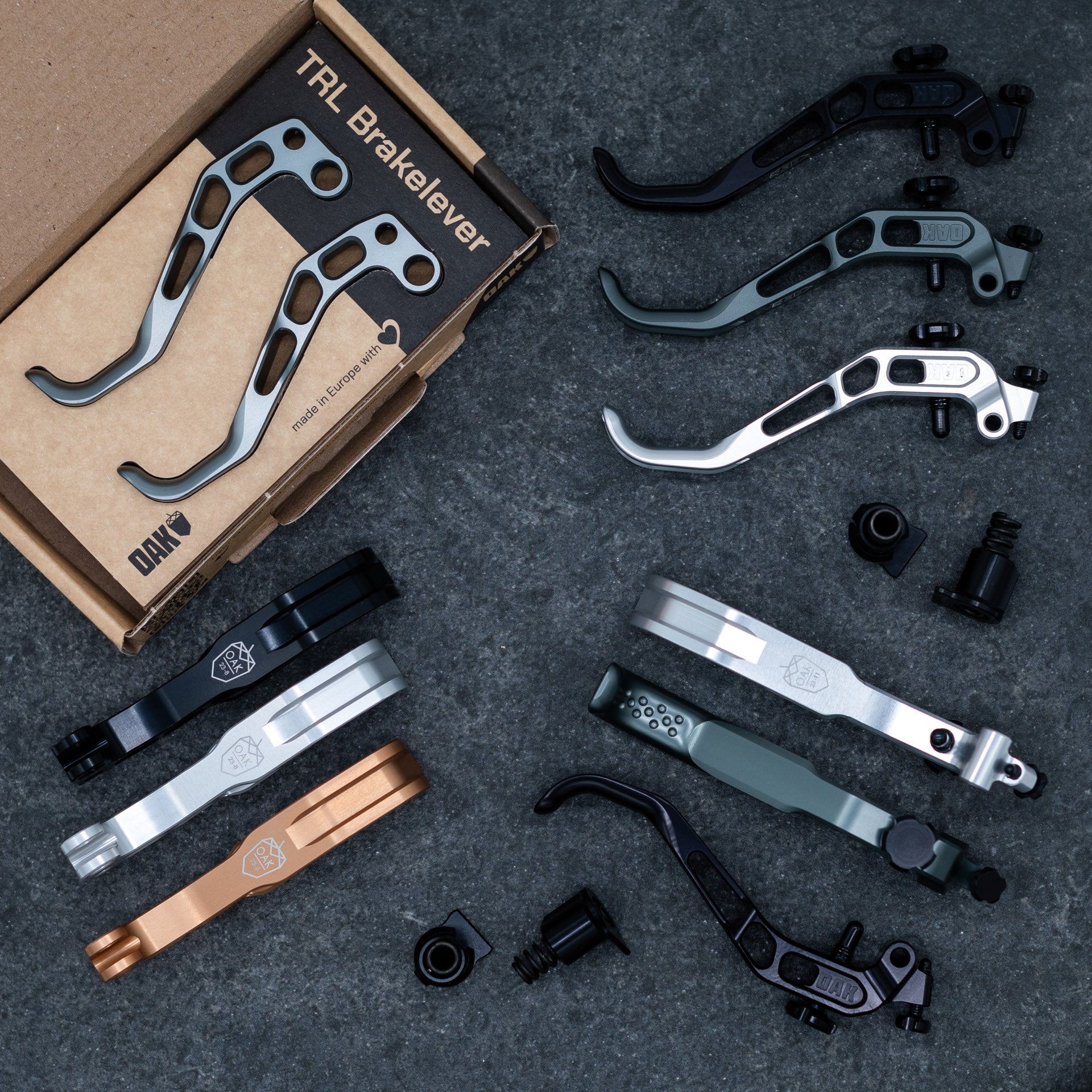 Silver OAK brake levers with cut-out holes on a box labeled 'Made in Europe' with OAK logo, surrounded by brake components.