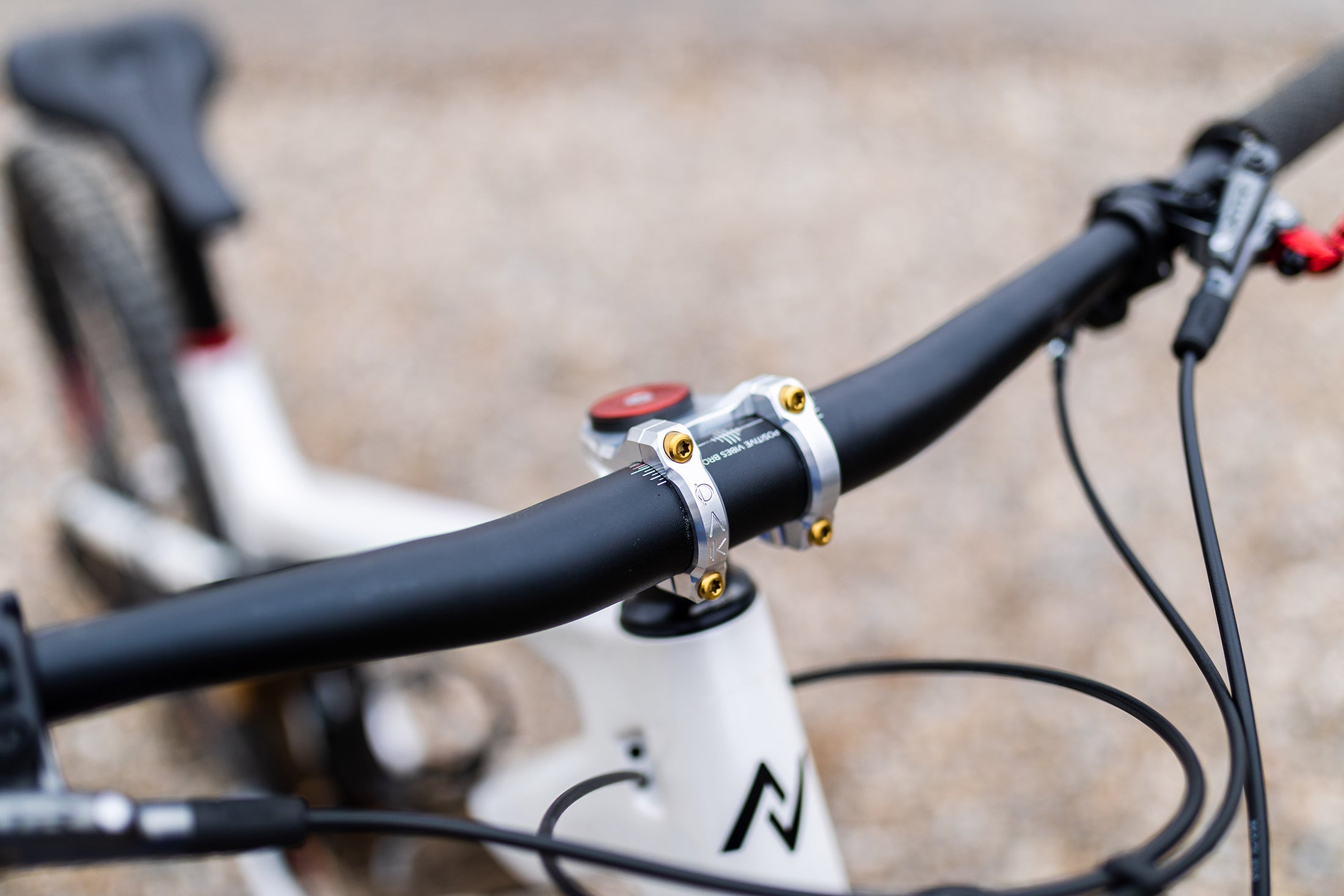 Close-up of white mountain bike handlebars with silver clamp, gold bolts, and "Positive Vibes Bro" text on the frame.